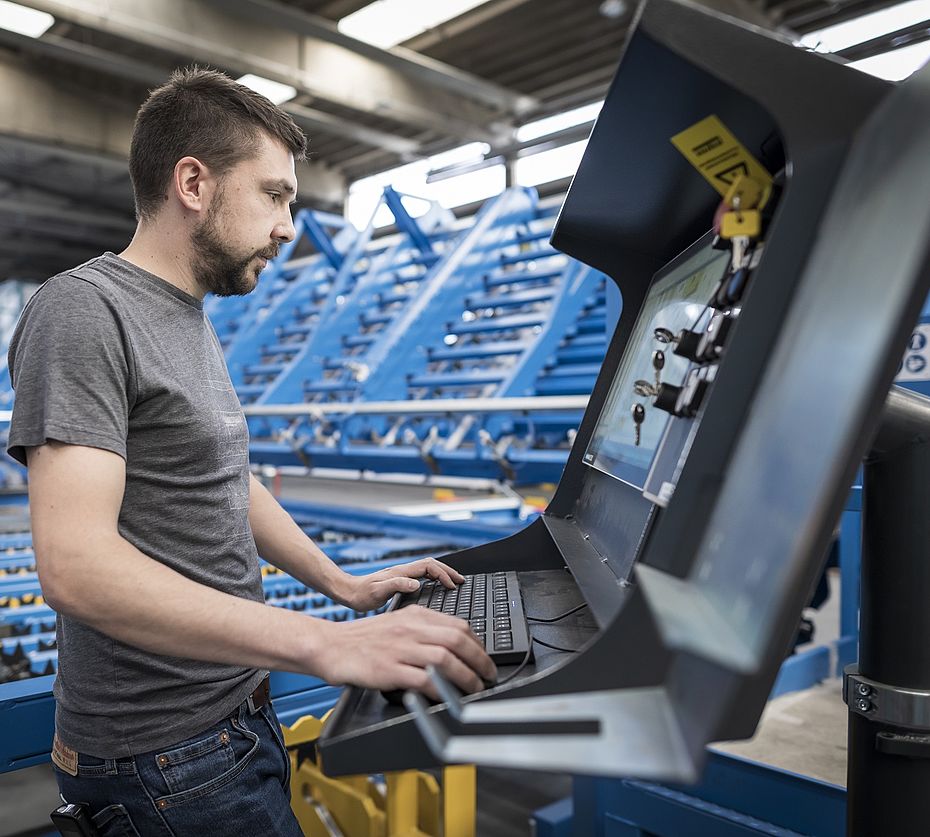 Mitarbeiter bedient industrielle Maschinensteuerung vor blauer Bewehrungsmaschine