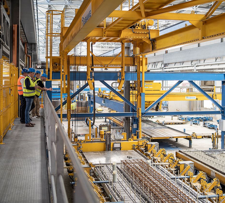 Collaboratori con caschi osservano impianto produzione EBAWE per produzione elementi prefabbricati in capannone